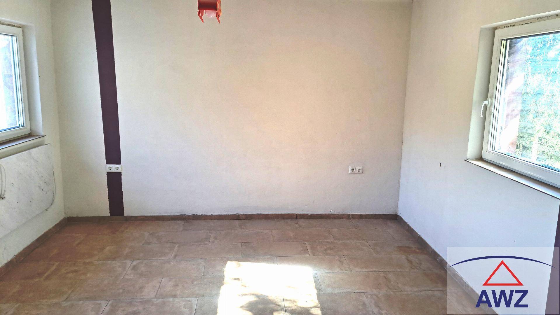 Heller, leerer Raum mit Fliesenboden und weißen Wänden, durch zwei Fenster gut mit Tageslicht versorgt.