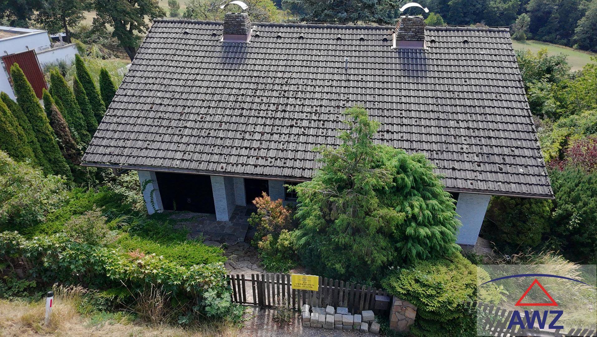 Luftaufnahme eines Einfamilienhauses mit Satteldach, umgeben von einem grünen Garten und Bäumen.