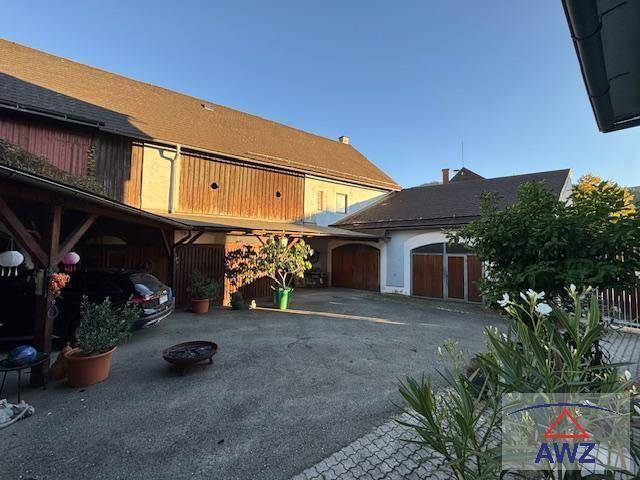 Ländliches Anwesen mit großem gepflastertem Hof, Carport und mehreren Garagen unter blauem Himmel.