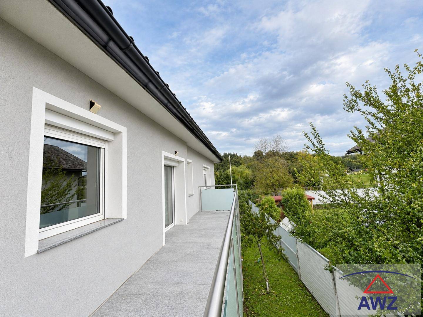 Langer Balkon mit modernem Glasgeländer und Blick ins Grüne unter einem bewölkten Himmel.