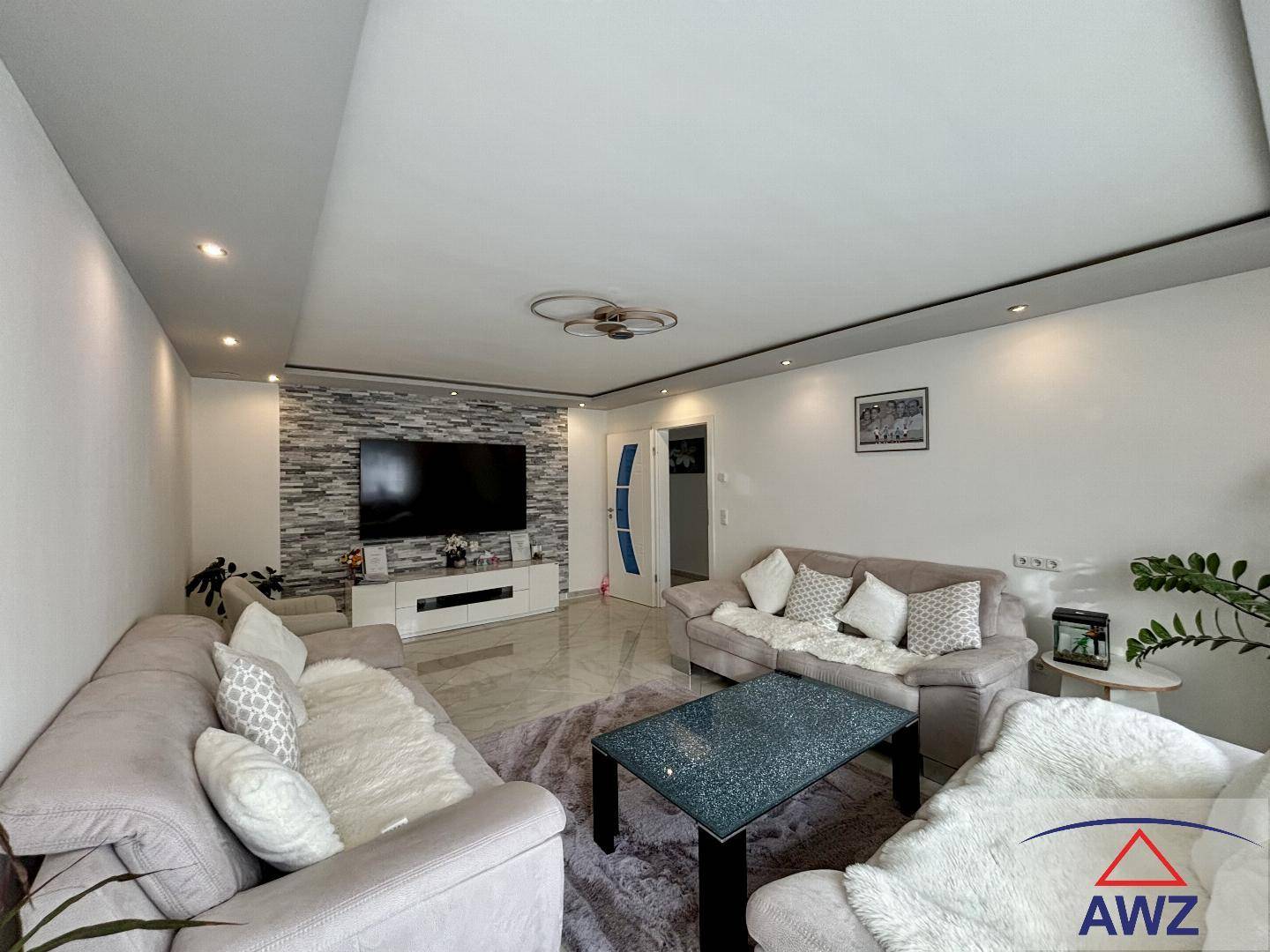 Modernes Wohnzimmer mit bequemen Sofas, großem Fernseher und einer dekorativen Steinwand als Akzent.