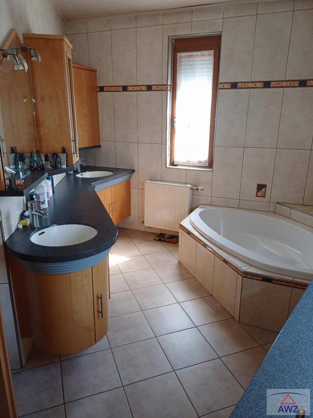Badezimmer mit Doppelwaschbecken, Eckbadewanne und Fliesenboden in neutralen Farbtönen.