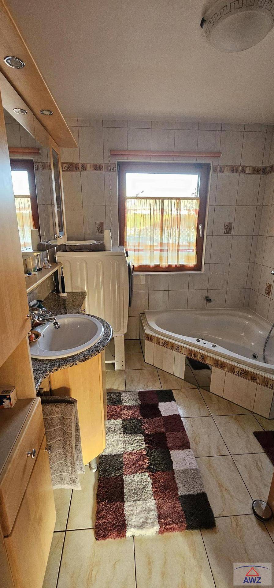 Gefliestes Badezimmer mit Badewanne, Einzelwaschbecken, Fenster und Waschmaschine.