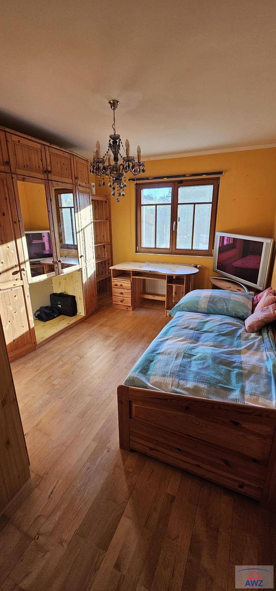 Schlafzimmer mit Einzelbett, Einbauschränken aus Holz, Schreibtisch und Kronleuchter.