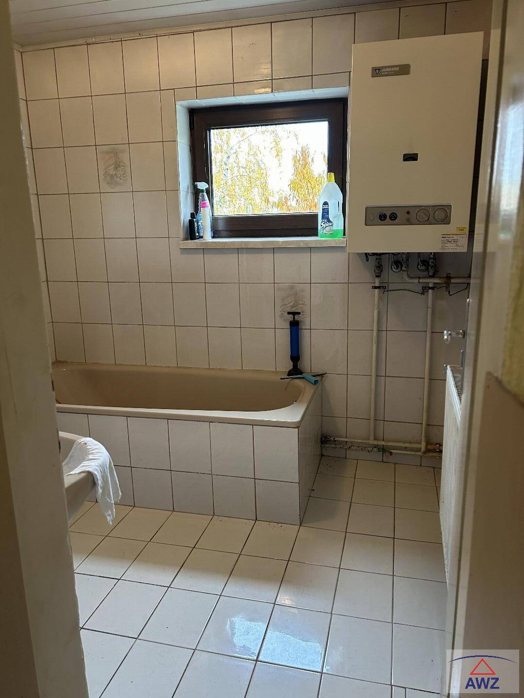 Gefliestes Badezimmer im Stil der 80er Jahre mit einer Badewanne, Fenster und einer Gastherme.