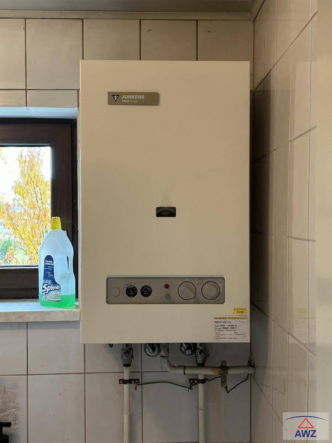 Eine Junkers Gastherme ist an einer gefliesten Wand neben einem Fenster installiert.