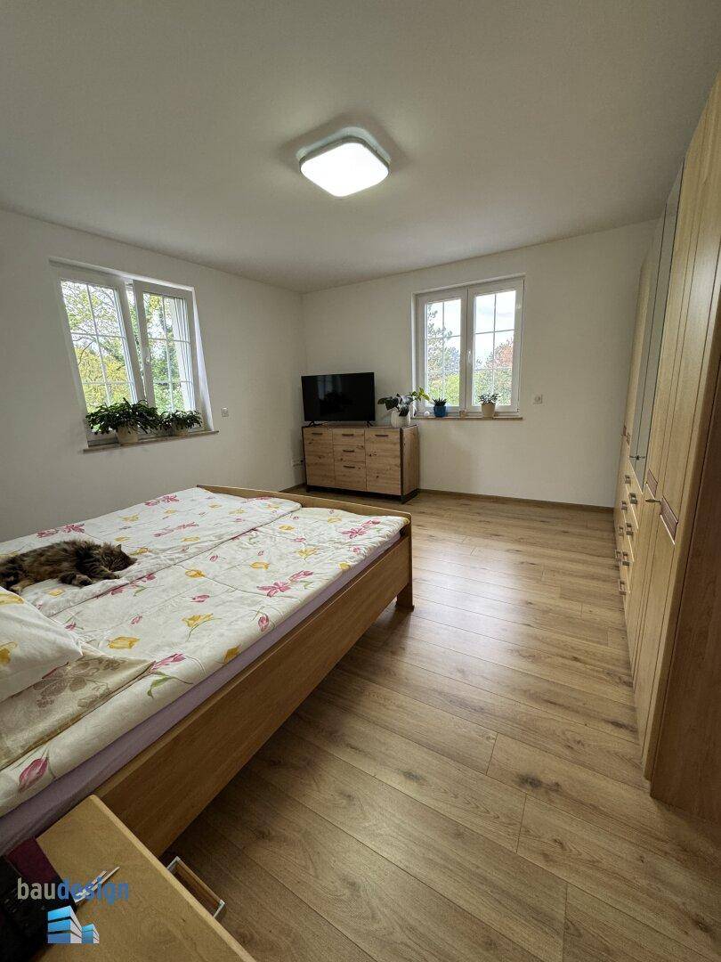 Helles Schlafzimmer mit Holzbett, Holzfußboden und zwei Fenstern für viel Licht.