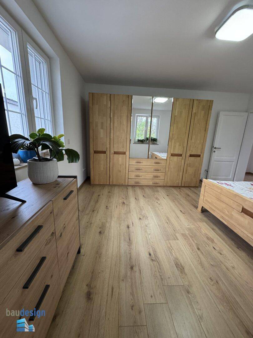 Geräumiges Schlafzimmer mit Holzfußboden, großem Spiegelschrank und viel Tageslicht.