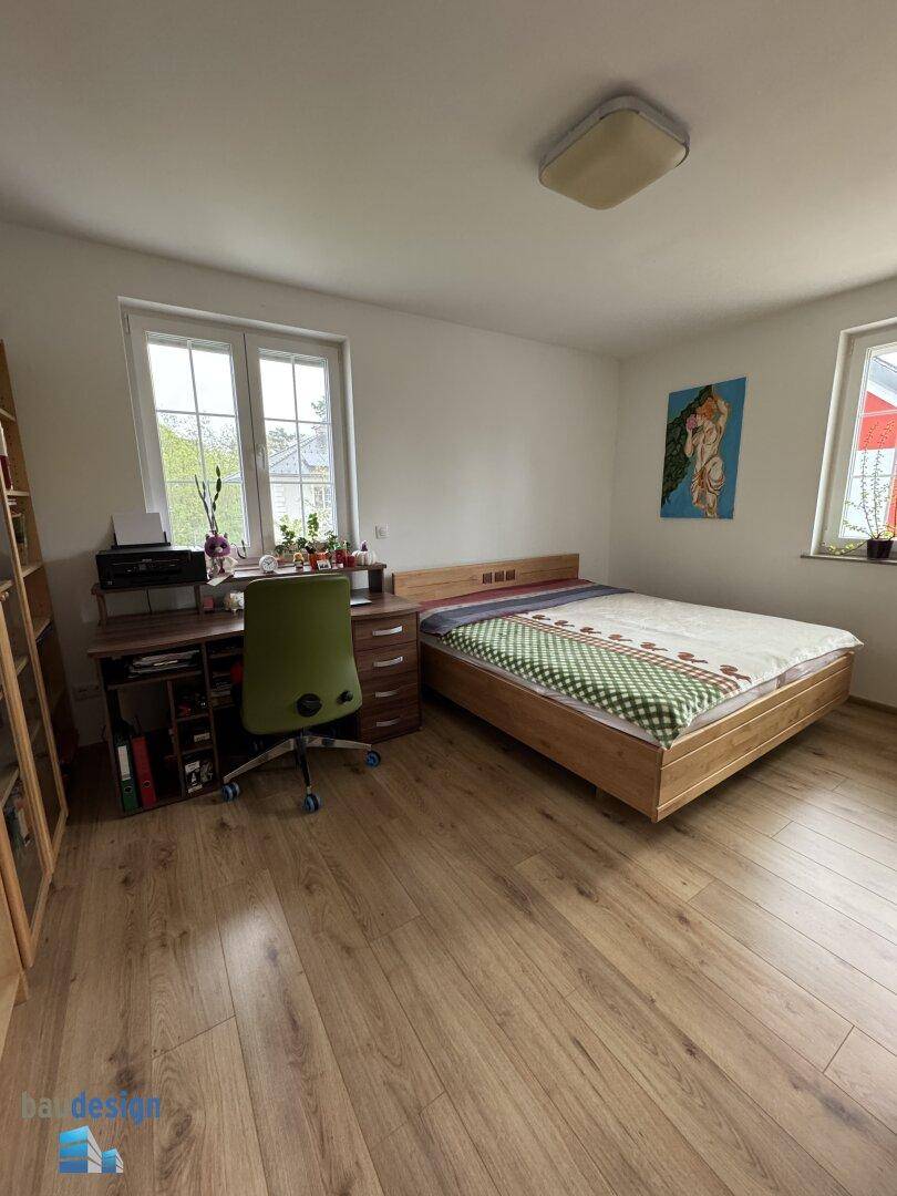 Helles Schlafzimmer, auch als Arbeitszimmer nutzbar, mit Holzboden und Fensterblick.