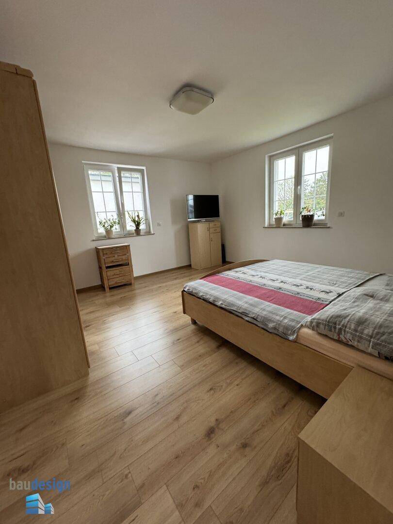Helles Schlafzimmer mit Holzboden, zwei Fenstern und einem Doppelbett in modernem Stil.