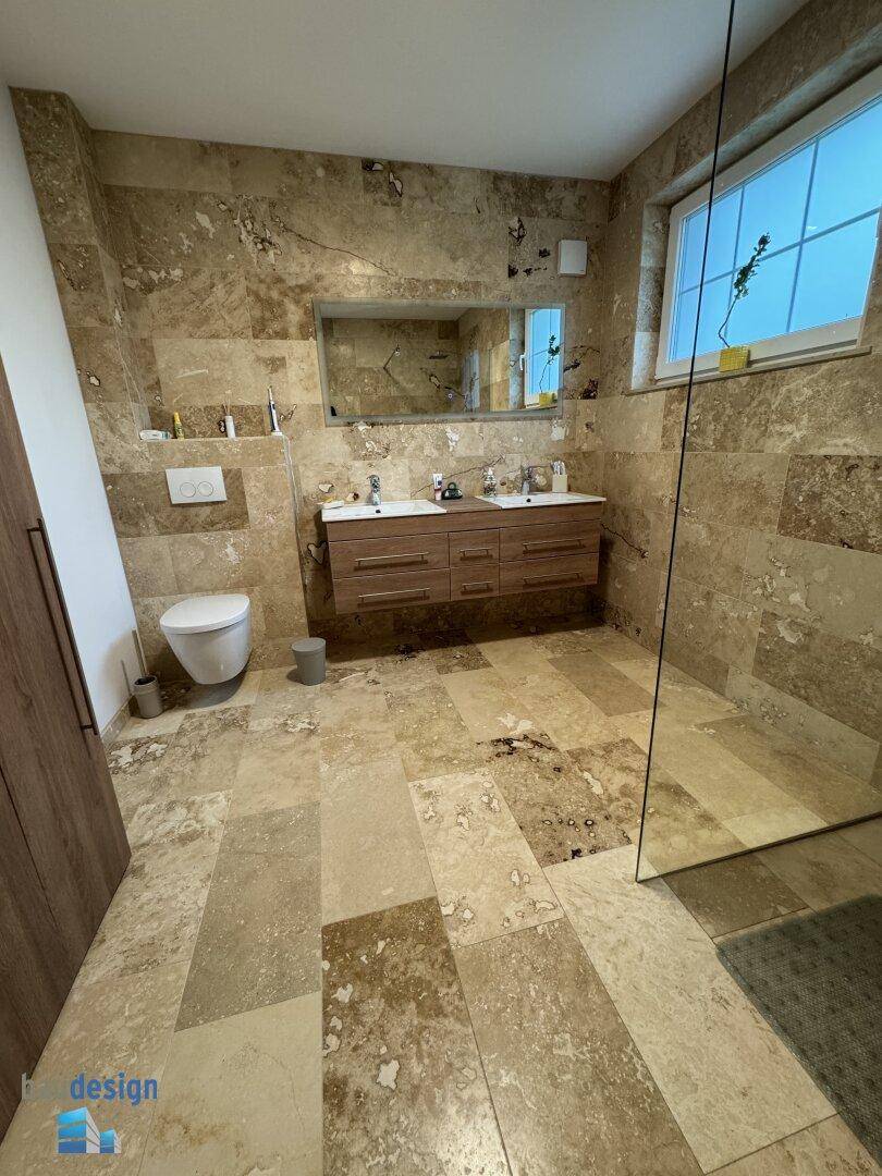 Geräumiges Badezimmer mit wandhängendem WC, Doppelwaschbecken und großer begehbarer Dusche.