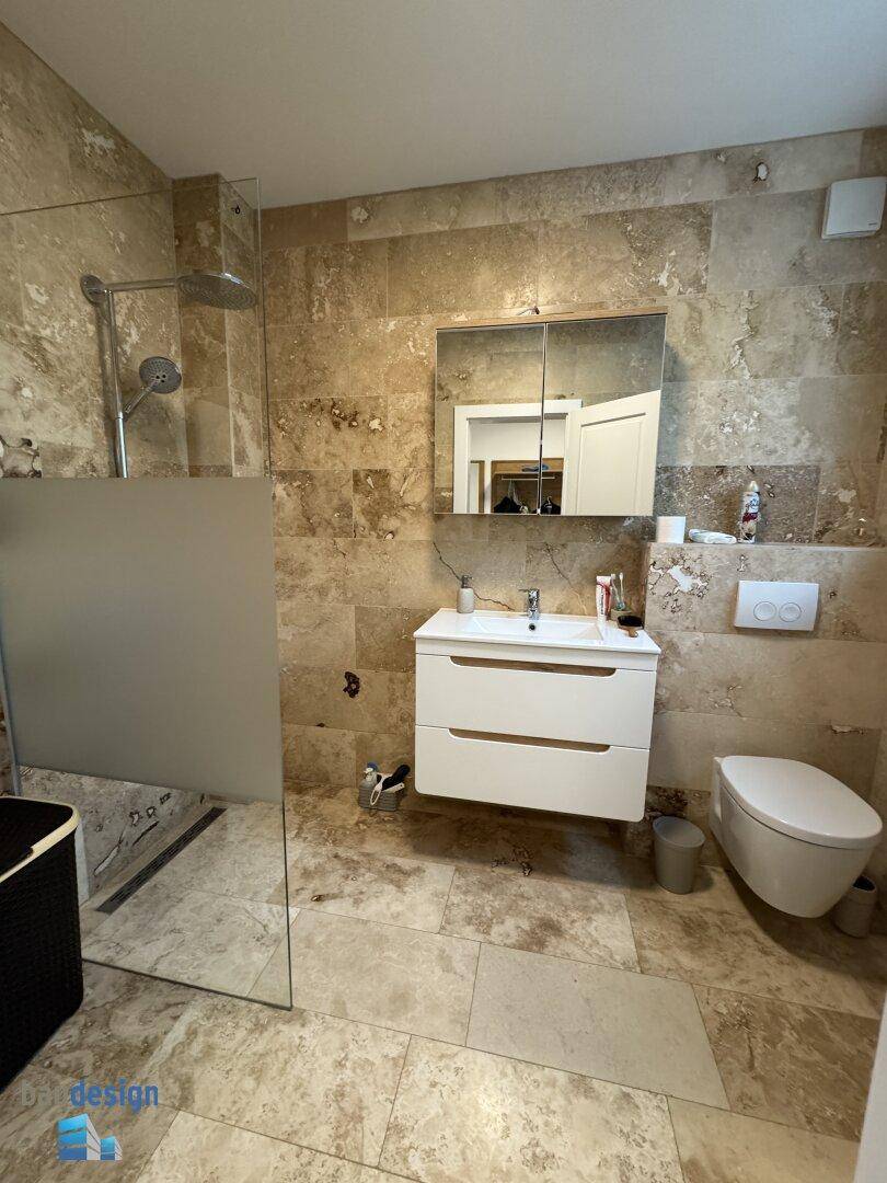Modernes Badezimmer mit beigefarbenen Fliesen, ebenerdiger Dusche und wandhängendem WC.