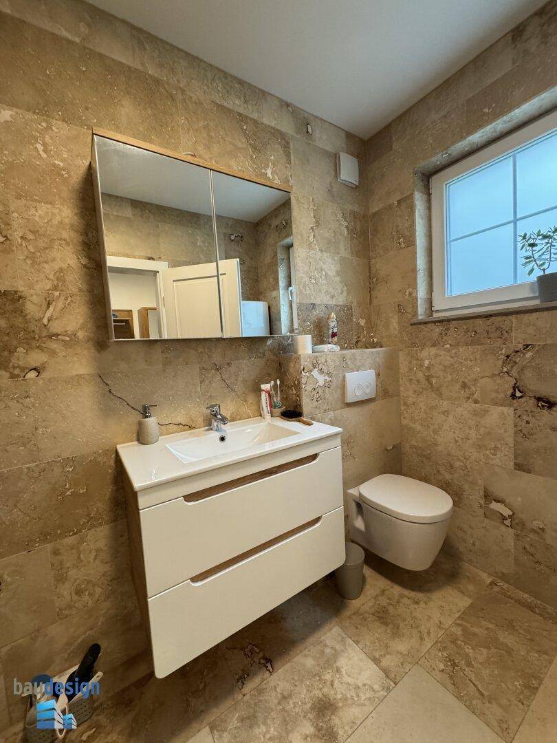 Helles Badezimmer mit Fenster, modernem Waschtisch, Spiegelschrank und WC.