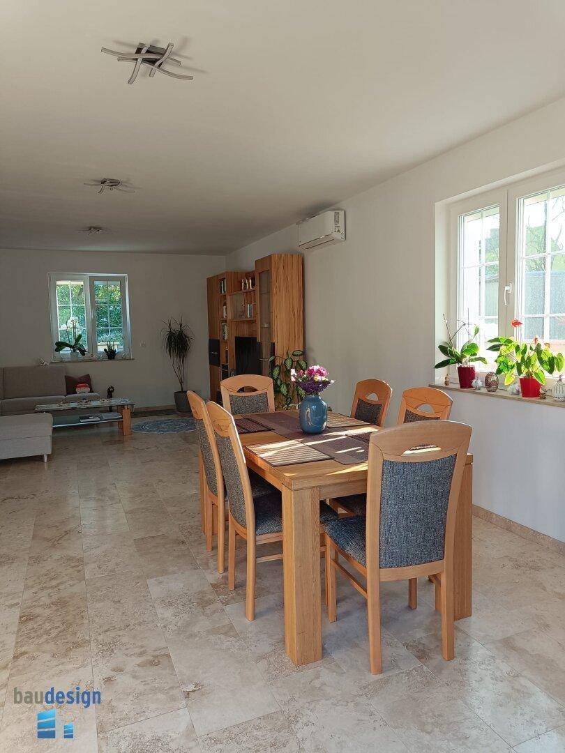 Heller Essbereich mit Holztisch und Stühlen, offen zum Wohnzimmer, mit Fliesenboden.