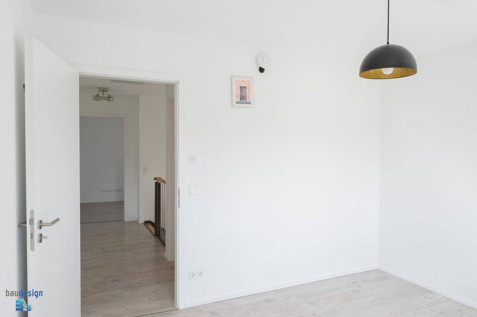 Helles Zimmer mit weiß gestrichenen Wänden und Laminatboden.