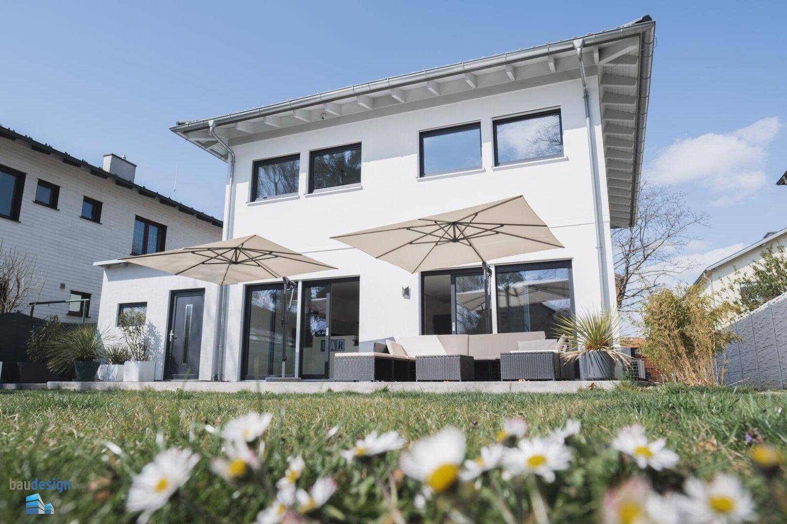 Moderne weiße Villa mit großer Terrasse, Garten und bequemen Outdoor-Möbeln unter Sonnenschirmen.