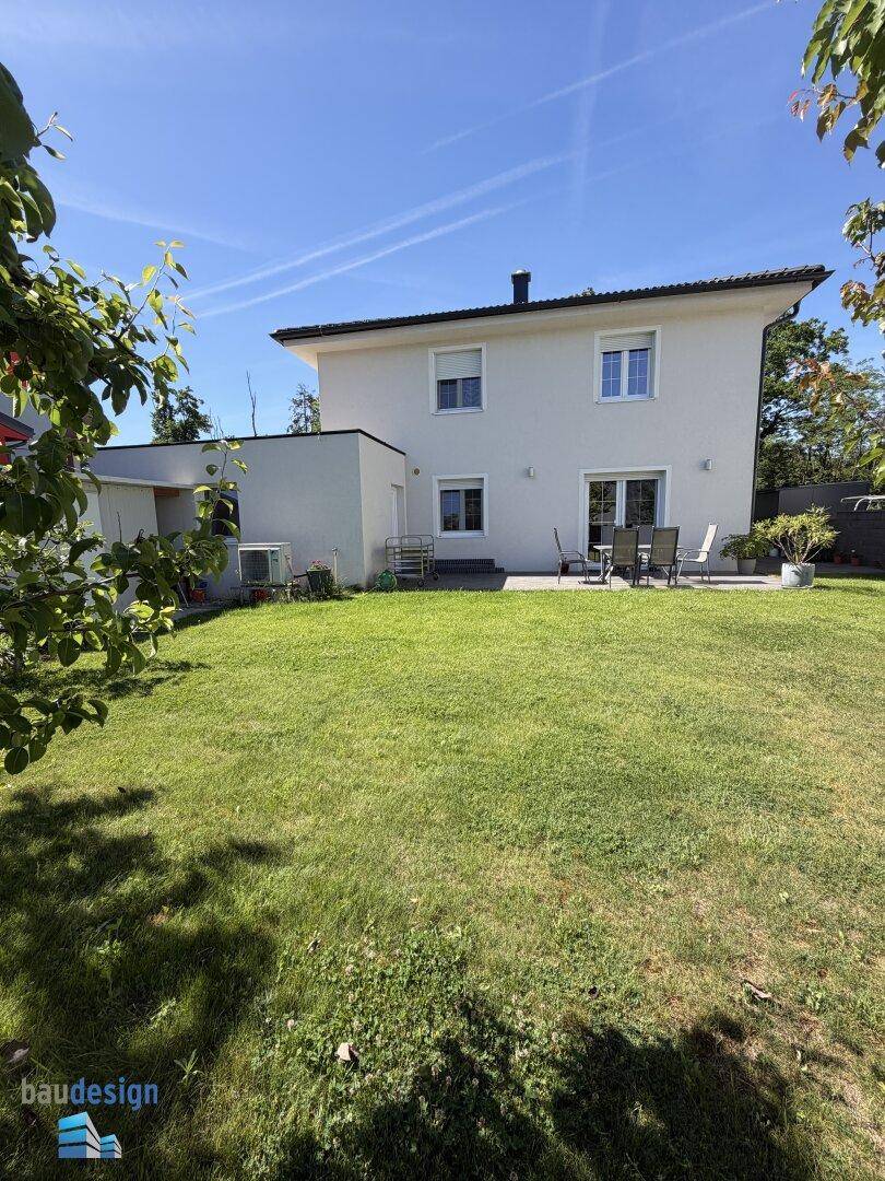 Hinteransicht eines modernen Einfamilienhauses mit großem Rasen und angrenzender Terrasse.