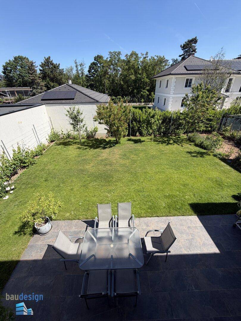 Übersicht der Terrasse mit Esstisch und dem angrenzenden, gepflegten Gartenbereich.