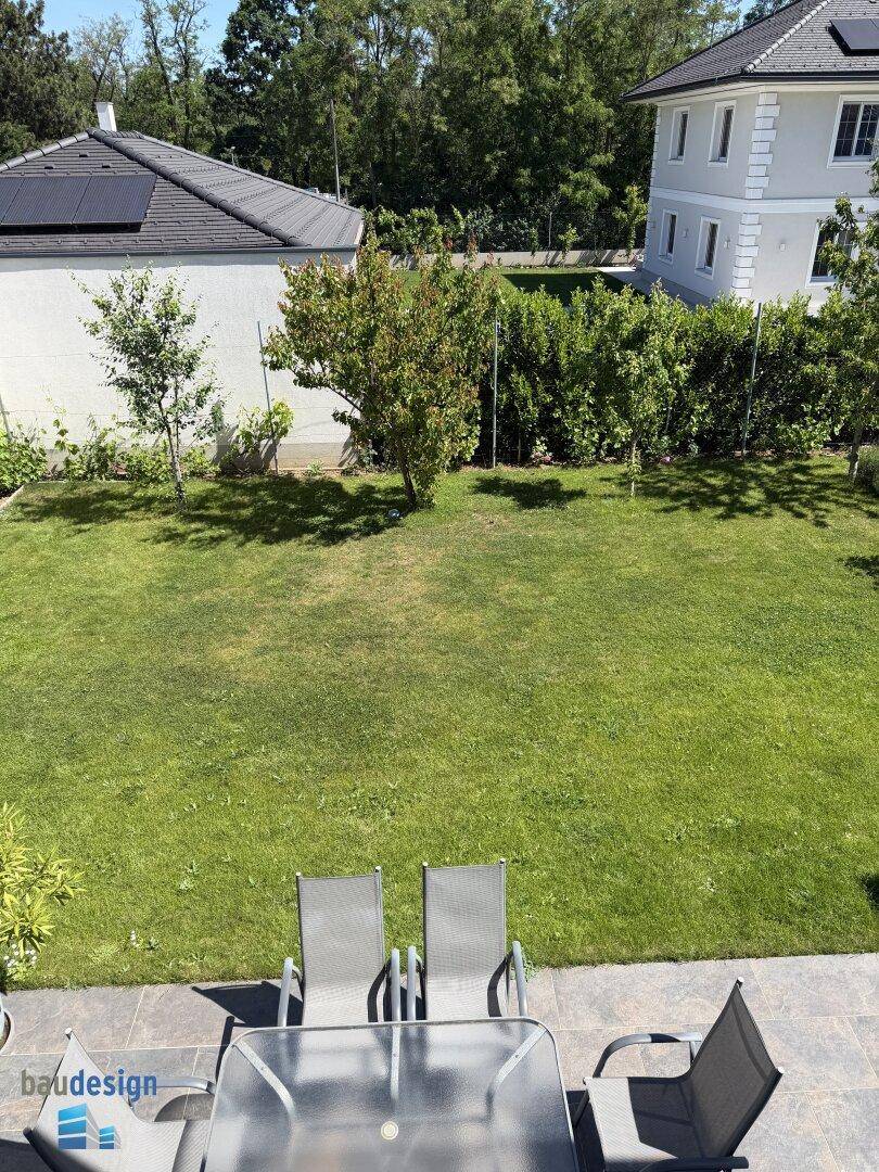 Detailansicht des Gartens mit Rasenfläche und der angrenzenden Terrasse im Sonnenlicht.