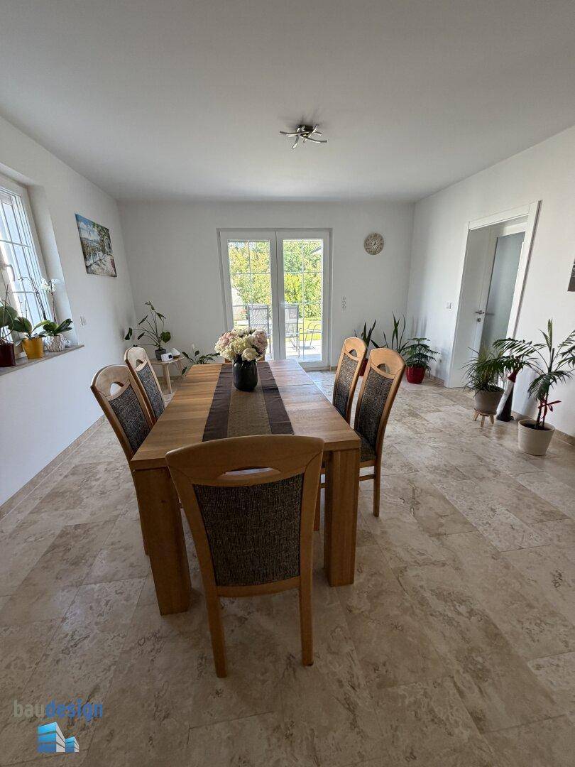 Essbereich mit Holztisch und Zugang zur Terrasse, umgeben von Pflanzen und Tageslicht.