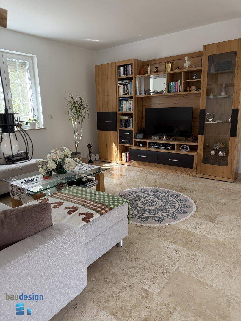 Helles Wohnzimmer mit beigem Fliesenboden, moderner Wohnwand und gemütlicher Sitzecke am Fenster.