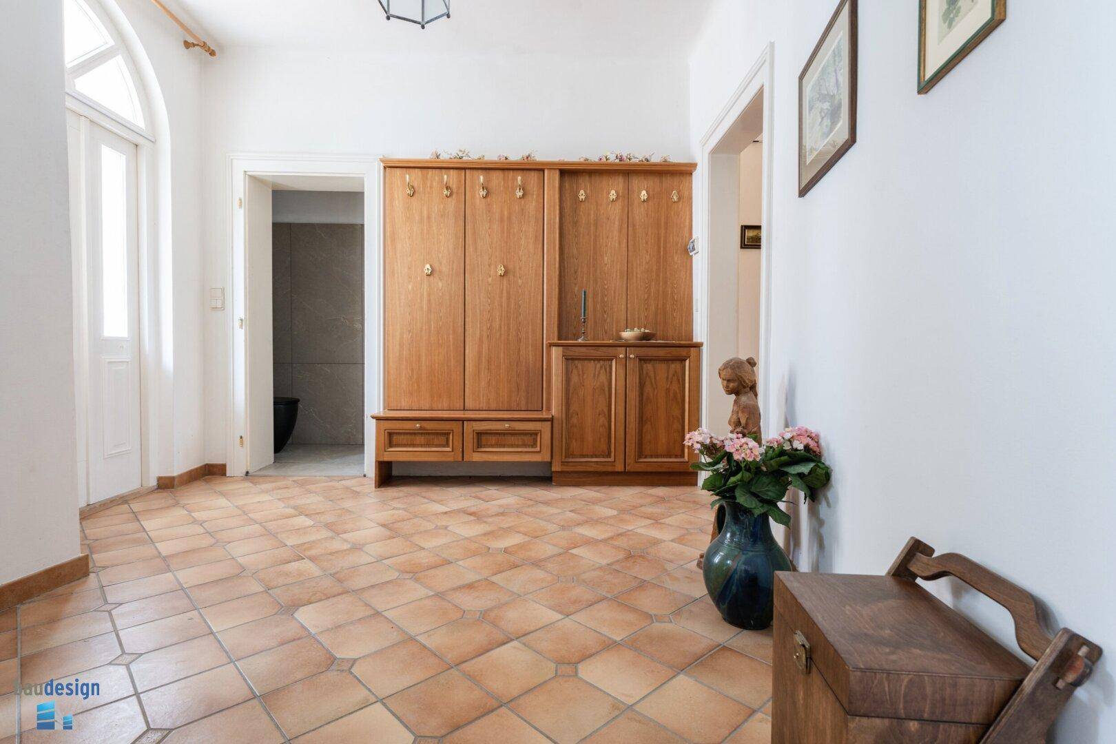 Eingangsbereich mit Terrakottafliesen, Holzgarderobe und Zugang zu weiteren Räumen.