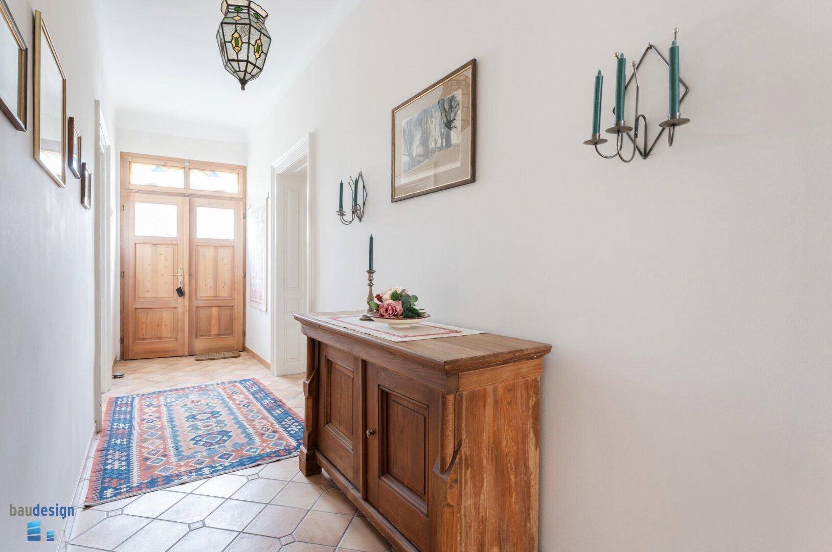 Heller Flur mit Terrakottafliesen, Holzkommode und traditionellem Teppich.