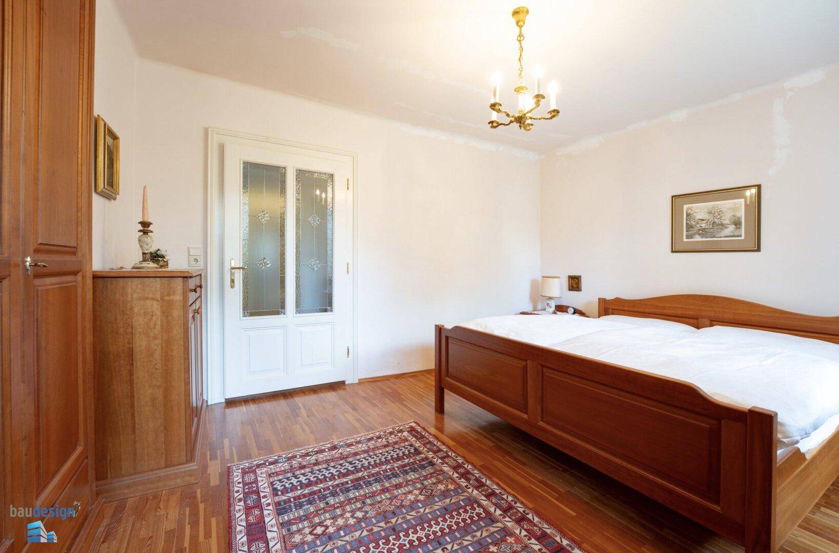 Schlafzimmer mit Holzbett, Parkettboden und traditionellem Teppich.