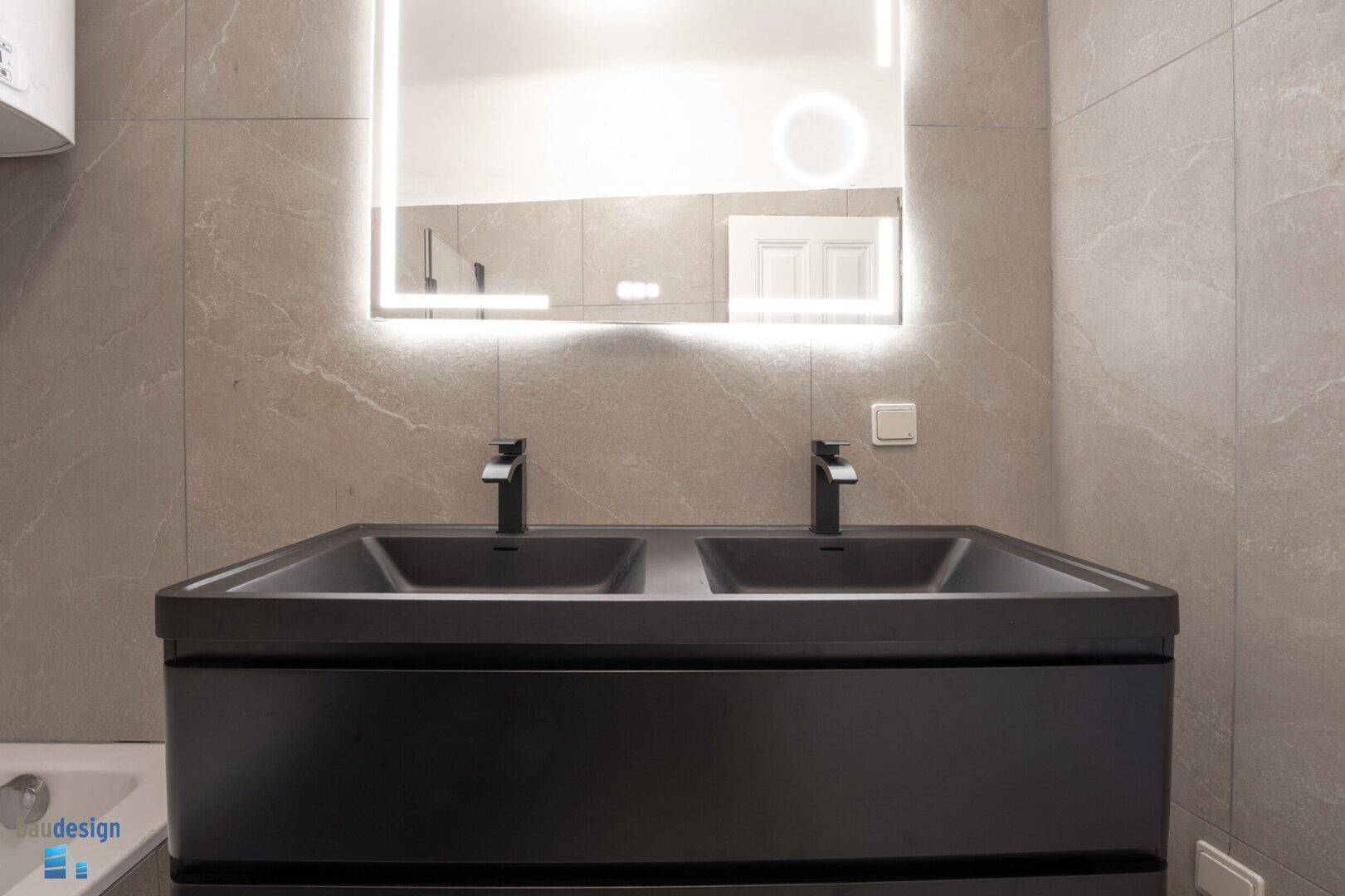 Moderner Doppelwaschtisch in Schwarz mit beleuchtetem Spiegel im Badezimmer.