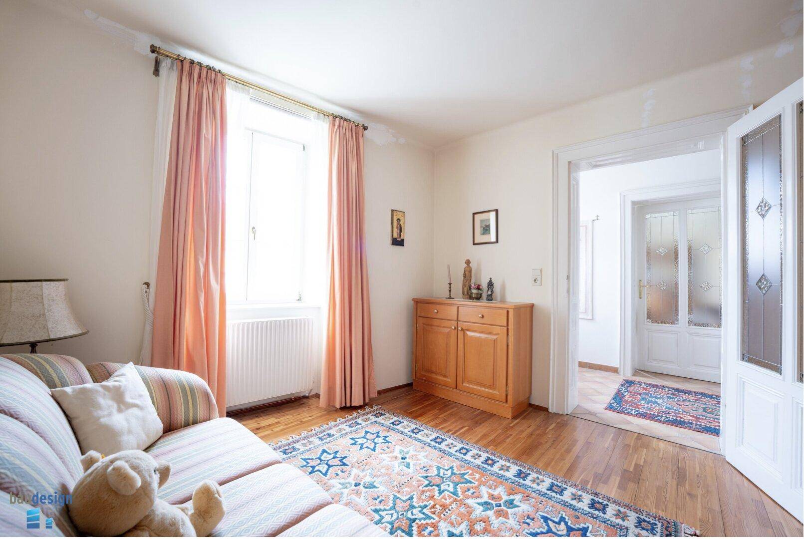Helles Wohnzimmer mit Sofa, Holzkommode und Zugang zu einem weiteren Raum.