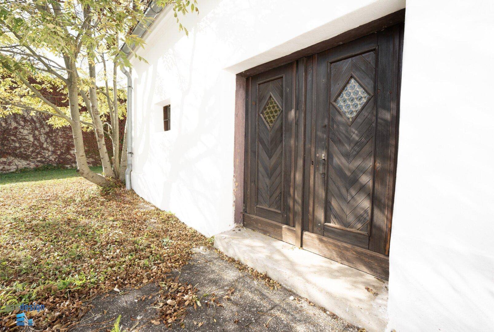 Rustikale Holztüren an einer weißen Fassade mit herbstlichem Laub auf dem Boden.