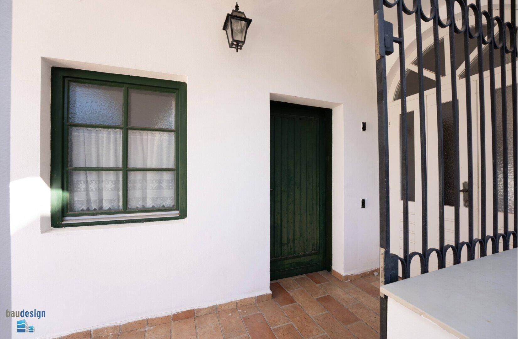 Weiße Fassade mit grünem Fenster und Tür, geschützt durch ein schmiedeeisernes Gitter.