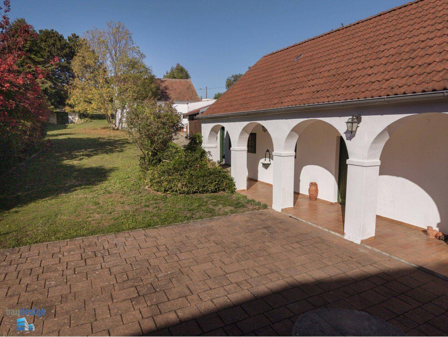 Großer gepflasterter Hof mit Arkaden und angrenzender Grünfläche.