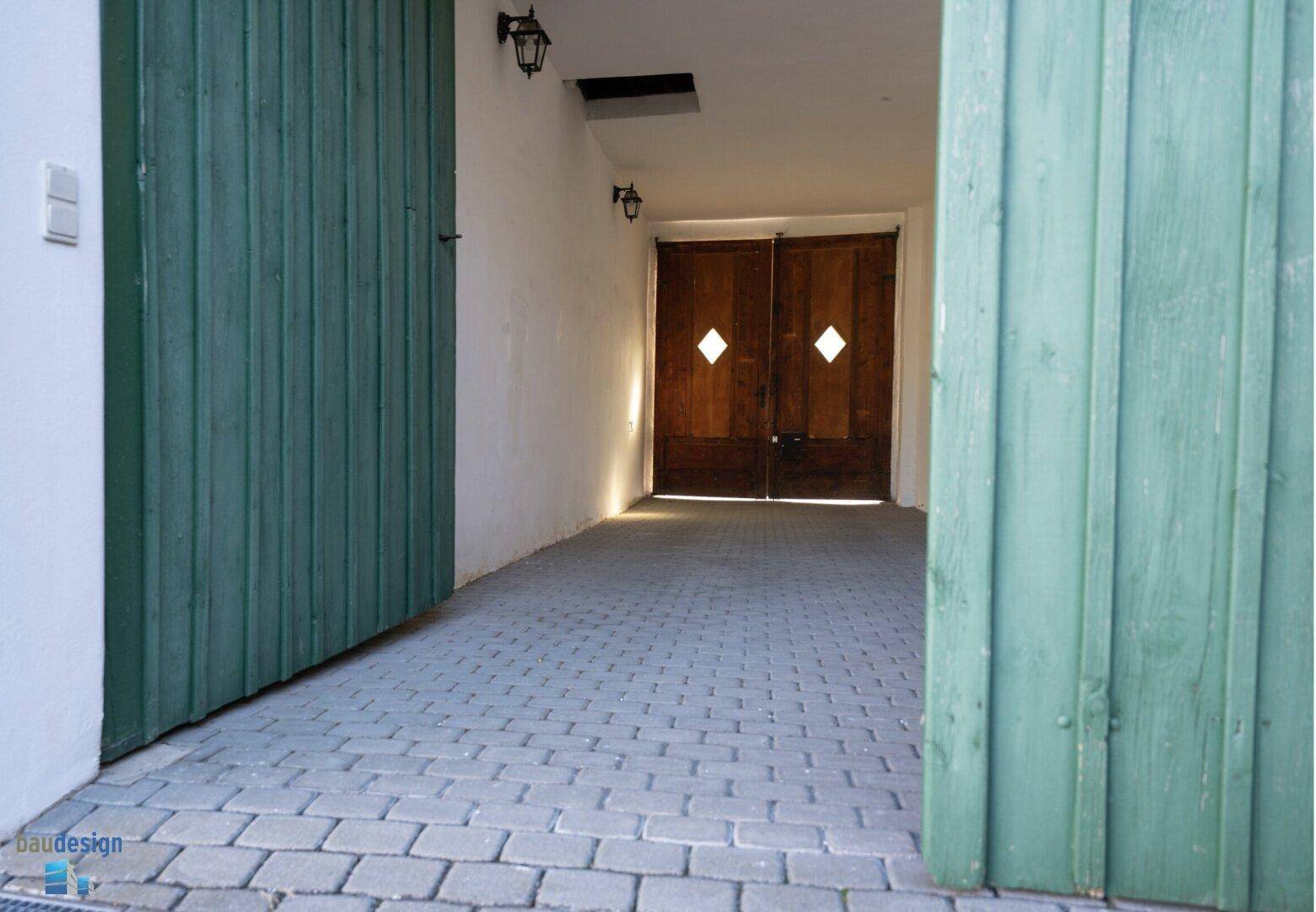 Eingang zu einer Garage oder Scheune mit großen Holztoren und Pflastersteinen.
