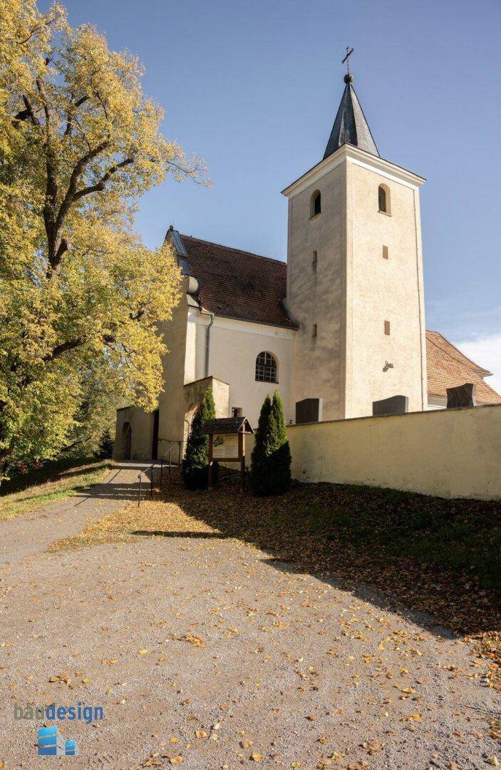 Historische Kirche mit Turm und einem großen Baum in herbstlicher Landschaft.