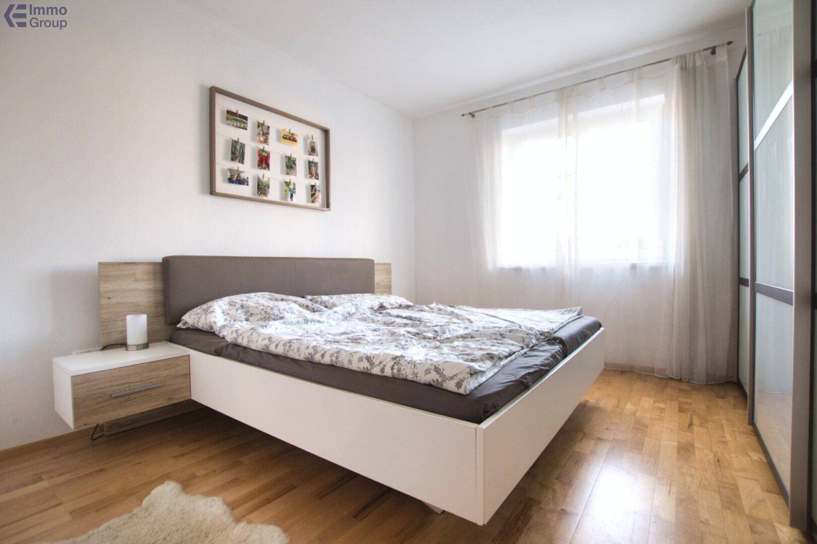 Helles Schlafzimmer mit Holzboden, modernem Bett und einem großen Fenster für viel Tageslicht.