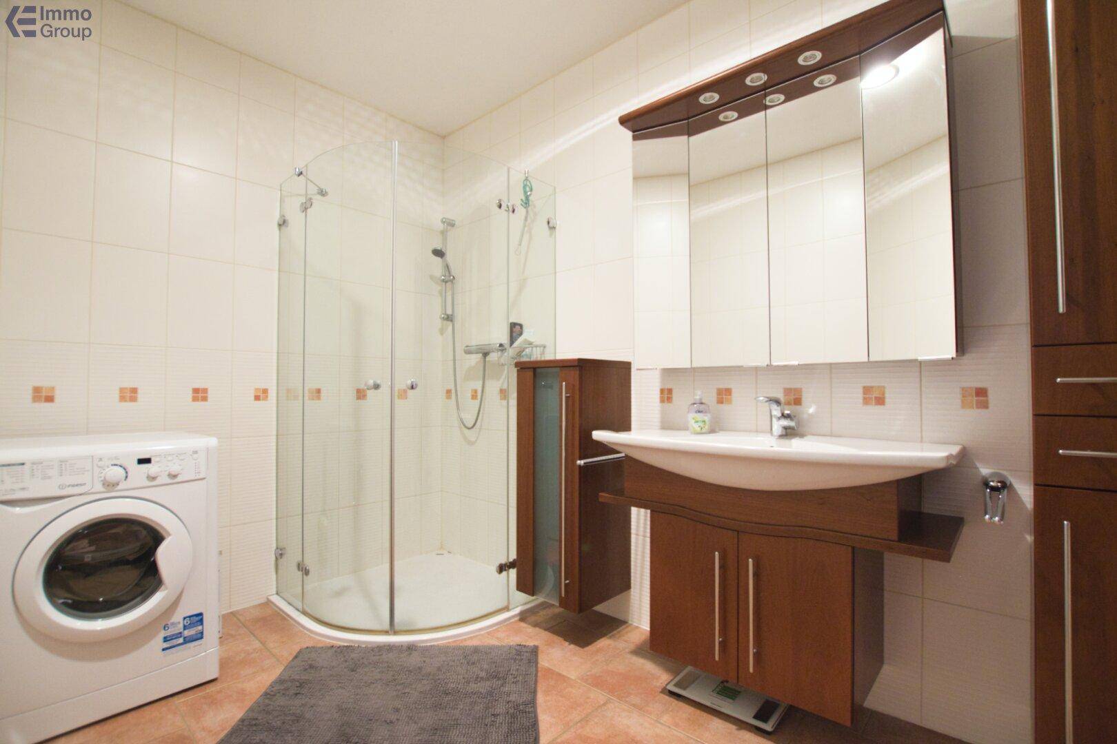 Badezimmer mit Eckdusche, Waschbeckenunterschrank aus Holz und einer Waschmaschine.