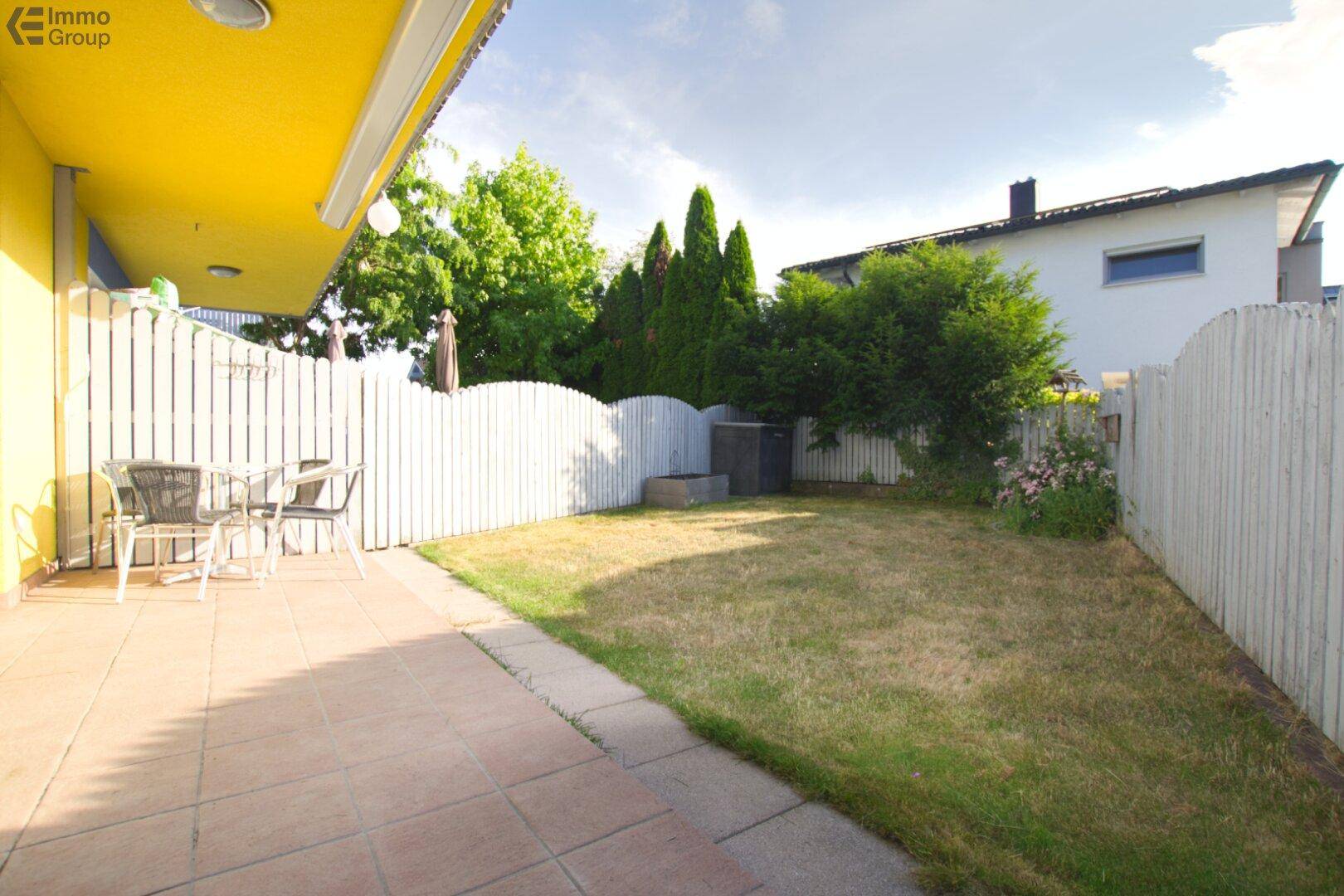 Sonniger Garten mit Rasenfläche, Terrasse und einem Zaun, ideal für Entspannung im Freien.