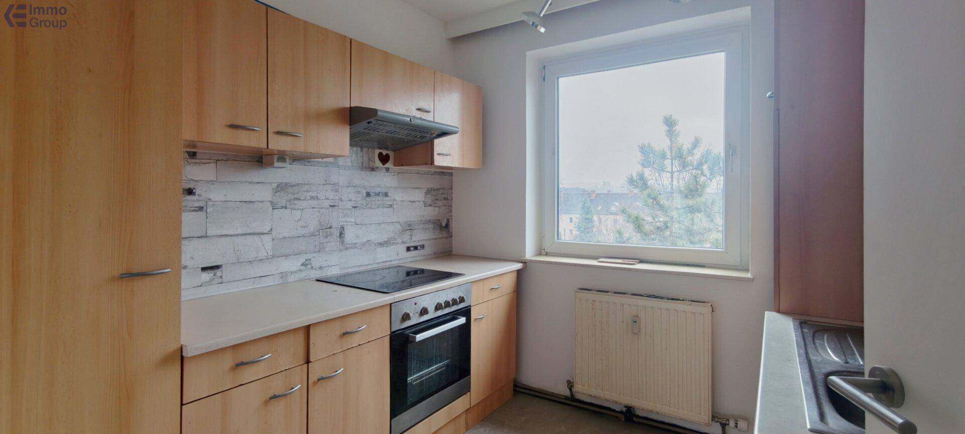 Helle Küche mit Holzschränken, integriertem Herd und Fenster mit Ausblick.