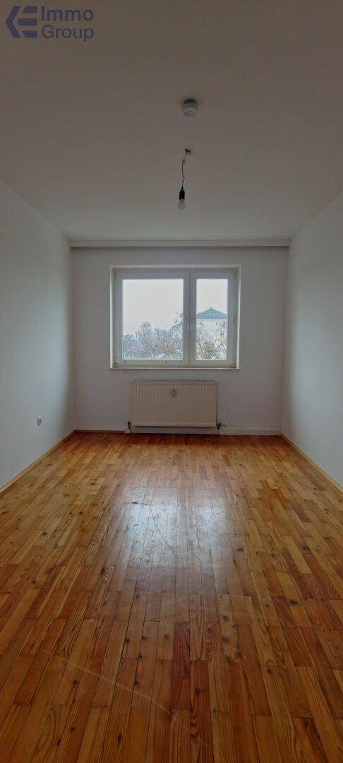 Heller, leerer Raum mit Holzboden und großem Fenster, ideal für individuelle Gestaltung.