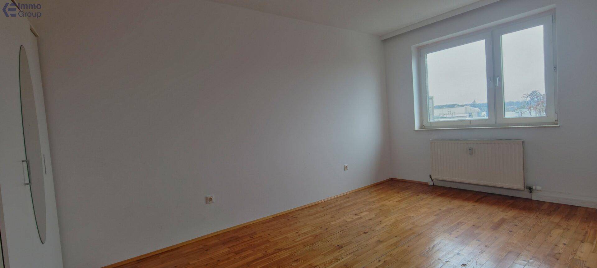 Leerer Raum mit Holzfußboden und großem Fenster, bietet viel natürliches Licht.