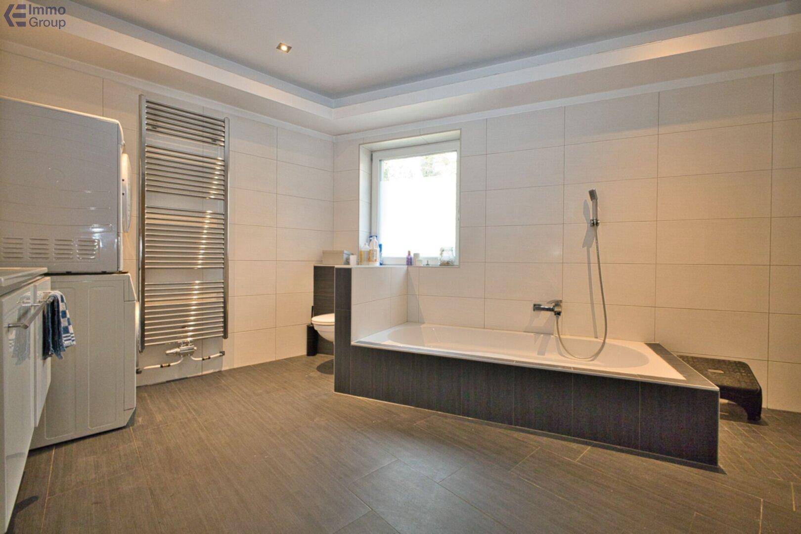 Modern gefliestes Badezimmer mit Badewanne, Fenster und praktischem Handtuchheizkörper.
