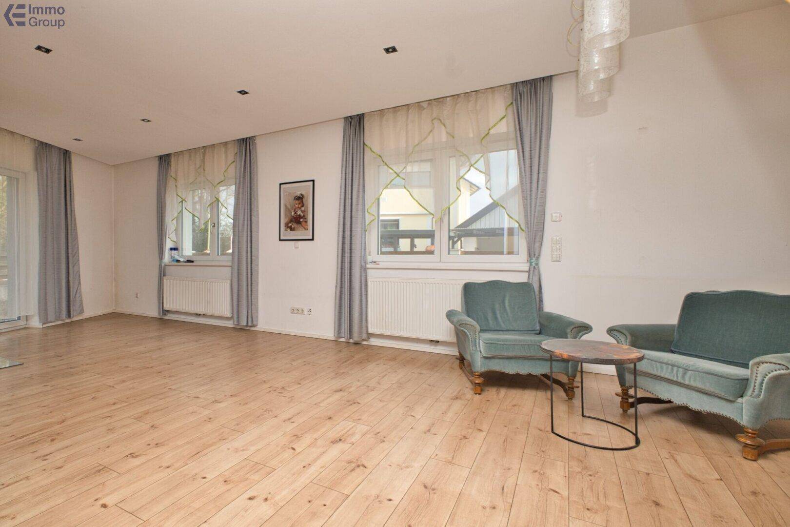 Helles Wohnzimmer mit Holzboden, großen Fenstern und Zugang zu einem Außenbereich.