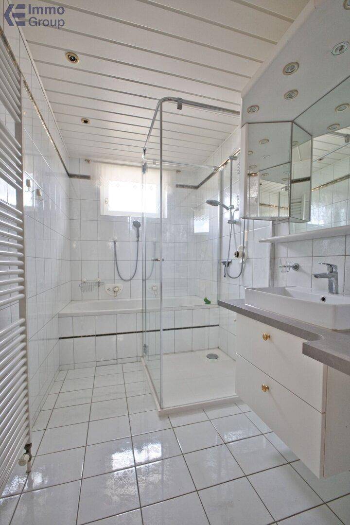 Helles Badezimmer mit weißen Fliesen, Badewanne, Duschkabine, modernem Waschtisch und beheiztem Handtuchhalter.