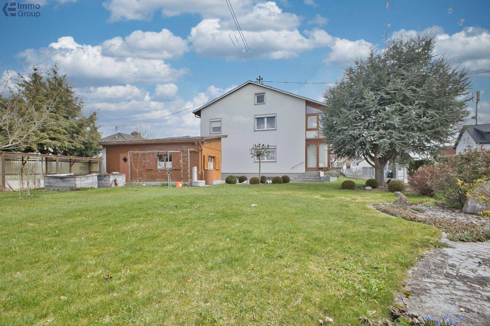 Großer, gepflegter Garten hinter dem Haus mit weitläufiger Rasenfläche und einem kleinen Nebengebäude.