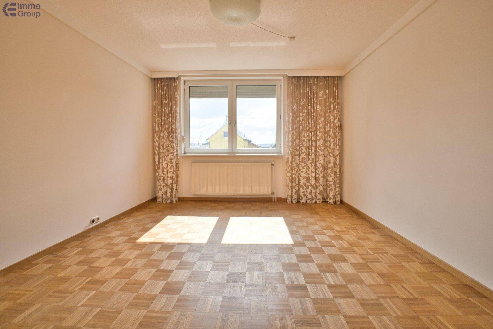 Geräumiges Schlafzimmer mit Parkettboden, großem Fenster und viel Tageslicht, bereit zur individuellen Gestaltung.