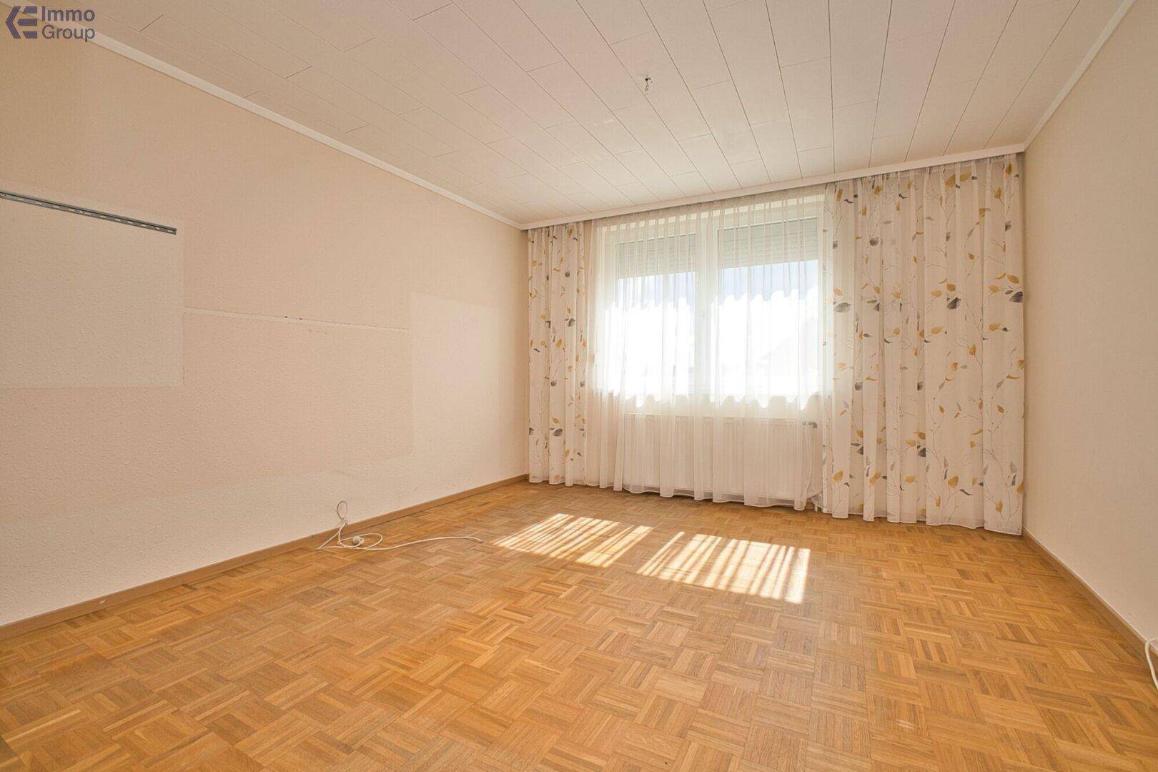 Helles Zimmer mit Parkettboden und großem Fenster, ideal als Schlaf- oder Arbeitszimmer nutzbar.