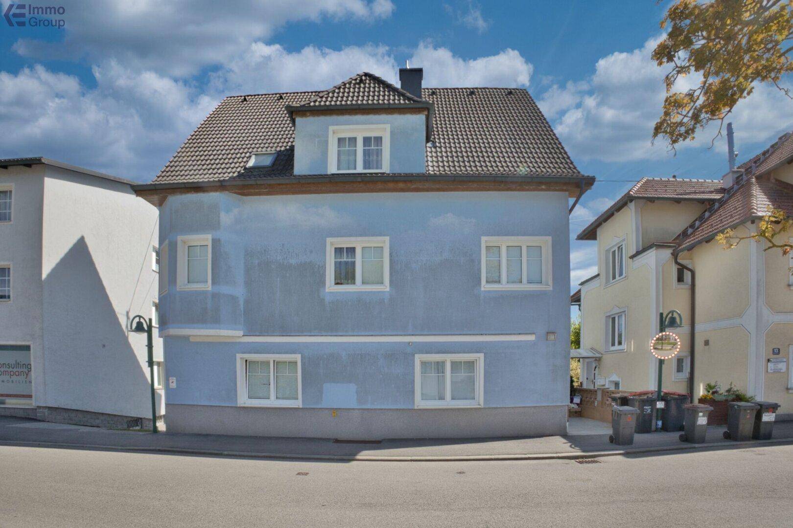 Ansicht des blauen Wohnhauses von der Straße mit Satteldach und mehreren Fenstern.