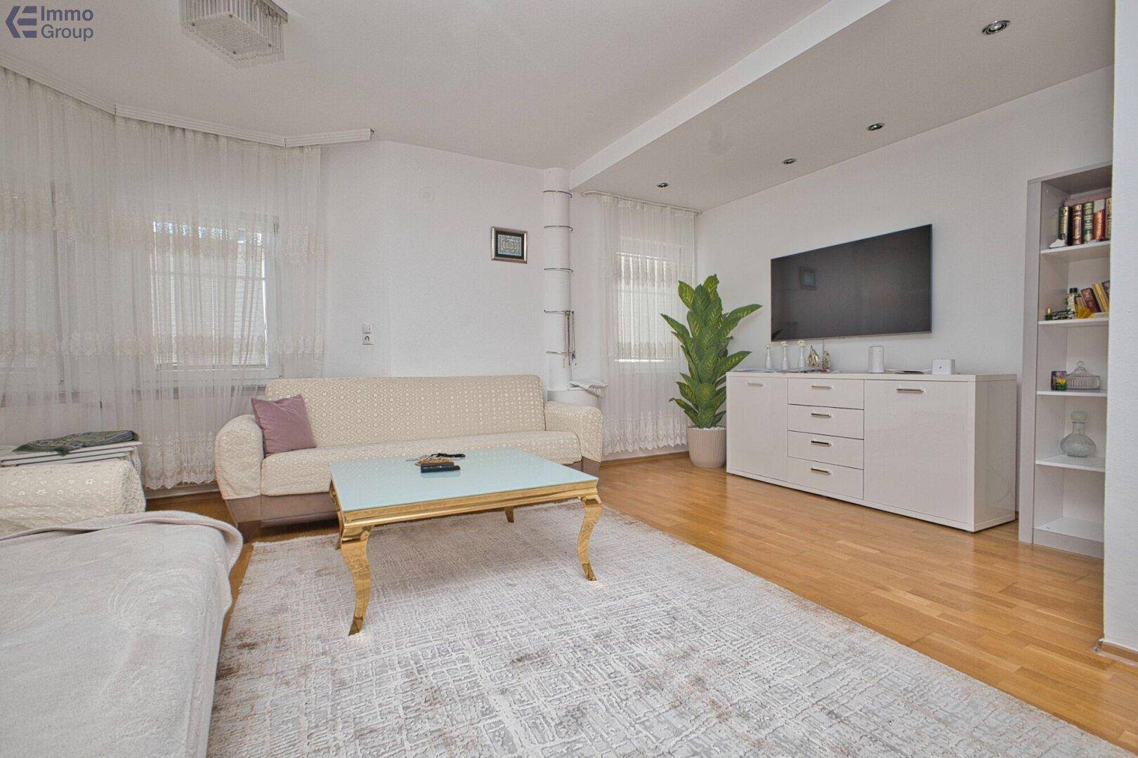 Helles Wohnzimmer mit beigem Sofa, Couchtisch, Fernseher und Holzboden.