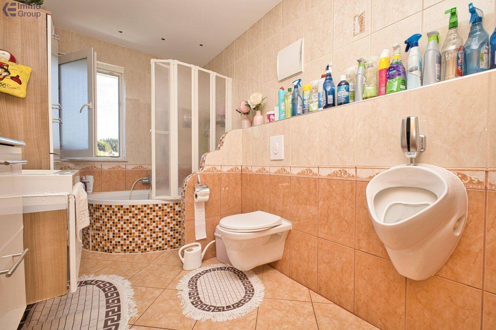 Badezimmer mit Urinal, Toilette, Eckbadewanne mit Duschvorhang und beigen Fliesen.